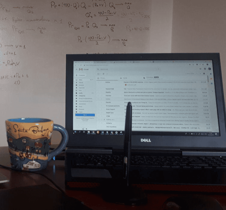 The author's Dell laptop in its original state, showing a cluttered interface on the screen. A whiteboard covered in complex formulas is in the background, representing the demanding and complex user experience before the Chrome OS Flex upgrade.